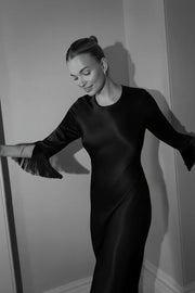 Black and white photo of a woman in a black party dress against a plain wall.