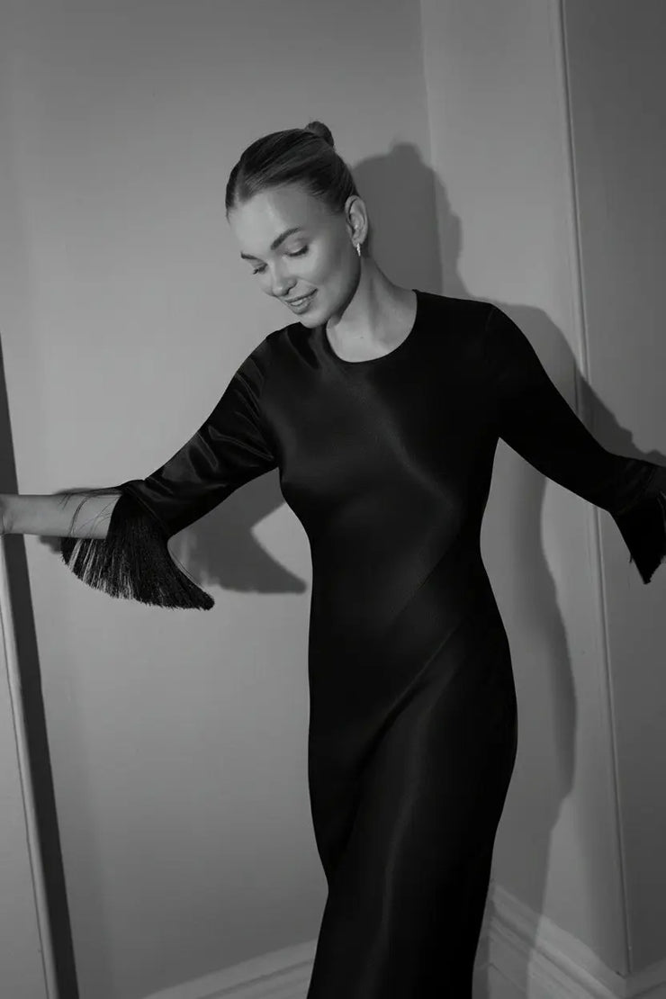 Black and white photo of a woman in a black party dress against a plain wall.