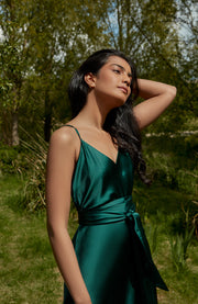 Woman in a green dress standing in a natural setting with trees and grass.
