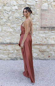 Woman in a rust-colored dress standing against a stone wall.