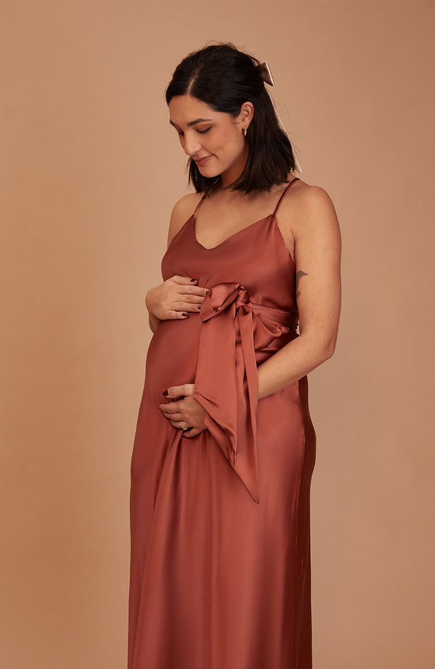 A pregnant woman wearing a bias cut satin slip bridesmaids dress in Terracotta. A beautiful rich cinnamon rose gold colour.