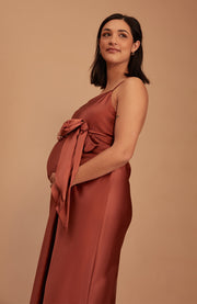 A pregnant woman wearing a bias cut satin slip bridesmaids dress in Terracotta. A beautiful rich cinnamon rose gold colour.