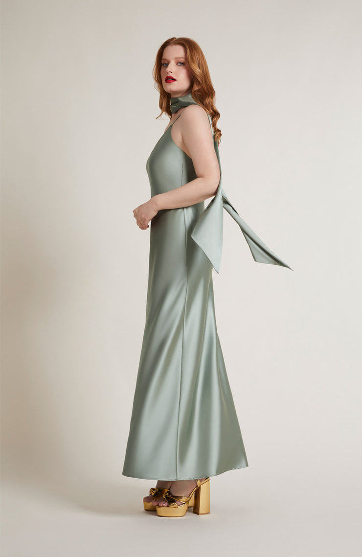 Woman wearing a light green halter neck dress with a bow detail on a plain background