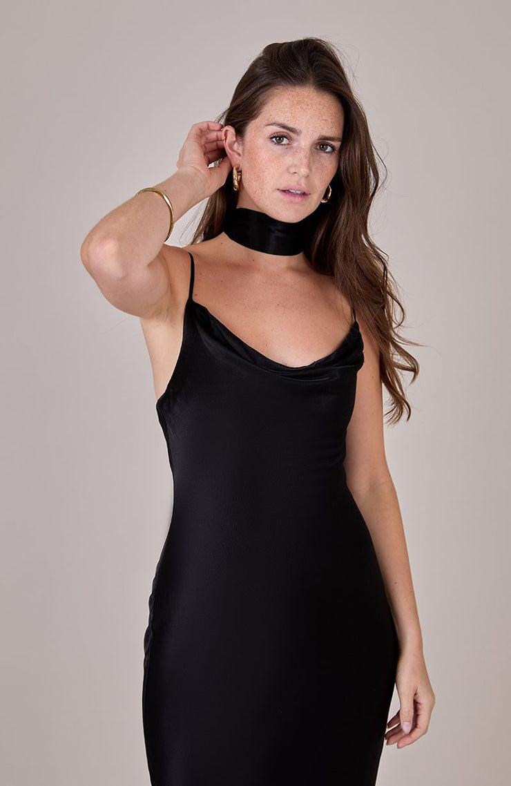 Woman wearing a black slip dress against a plain background