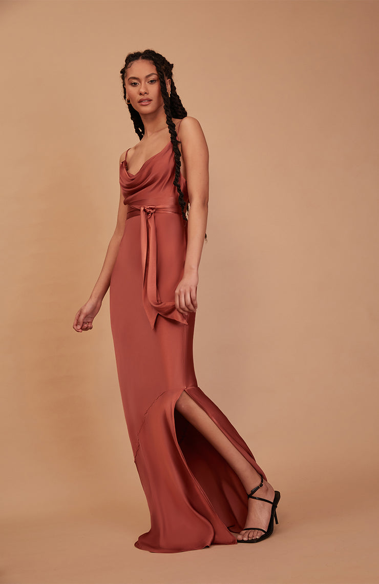 Woman wearing a rust-colored gown with a slit on a beige background
