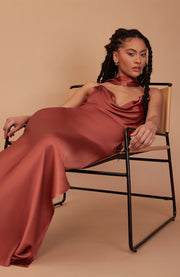 Woman in a rust-colored dress sitting on a chair against a beige background
