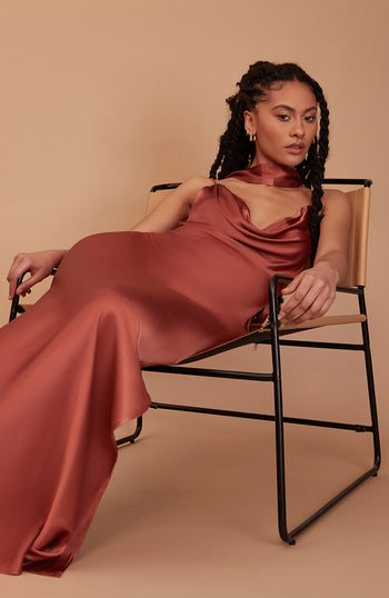 Woman in a rust-colored dress sitting on a chair against a beige background