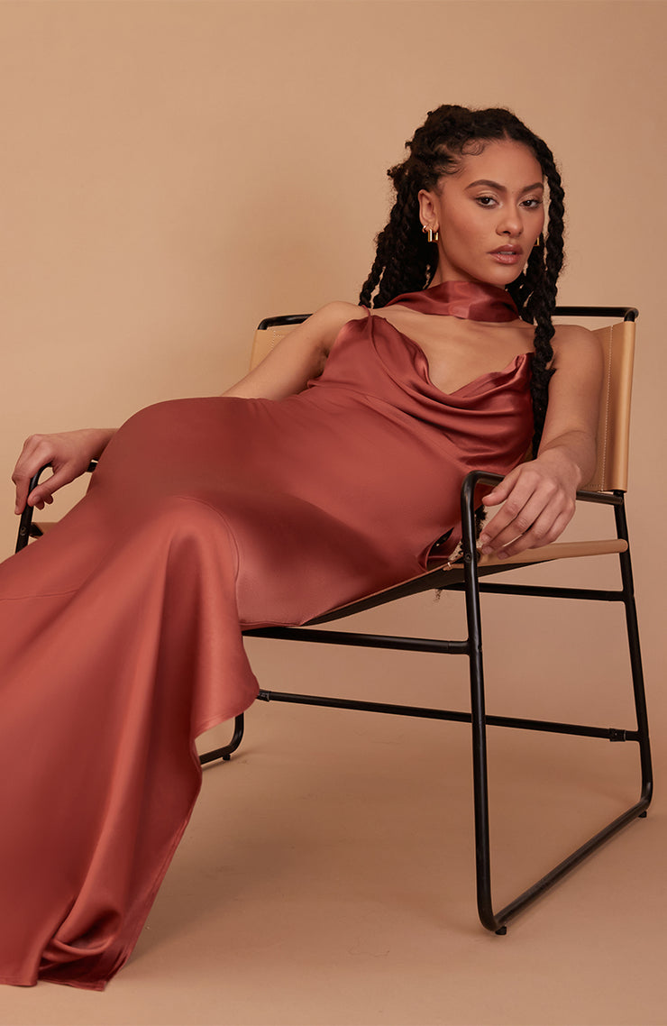 Woman in a rust-colored dress sitting on a chair against a beige background