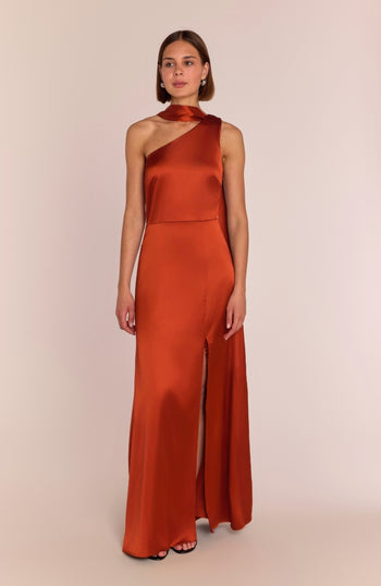 Woman wearing a rust-colored one-shoulder jumpsuit on a beige background