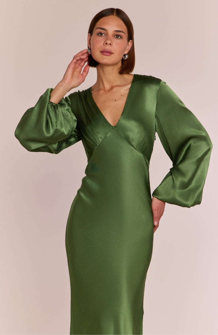 Woman wearing a green satin dress with long sleeves against a beige background