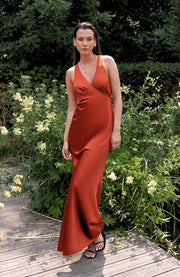 Woman in a rust-colored dress standing on a wooden path with greenery around