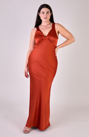 Woman wearing a rust-colored satin evening gown on a plain background