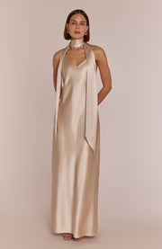 Woman wearing a long, elegant gold dress with a plain background