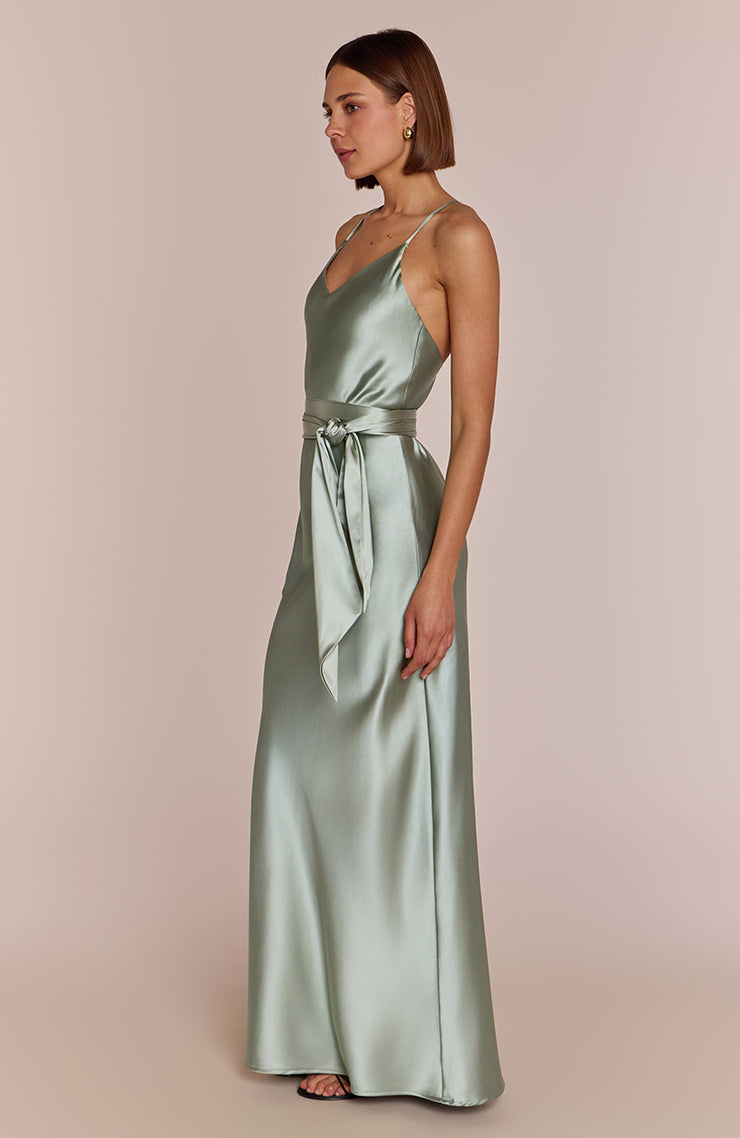 Woman wearing a long satin dress with a belt on a plain background