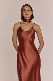 Woman wearing a rust-colored satin slip dress against a plain background