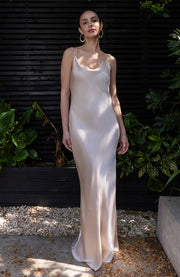 Woman in a white slip dress standing outdoors with greenery in the background