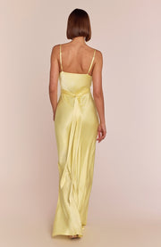 Woman wearing a light yellow satin gown with thin straps on a beige background
