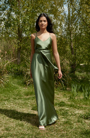 Woman in a green dress standing in a natural setting with trees and grass.