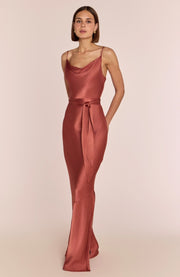 Woman wearing a rust-colored satin dress on a light pink background