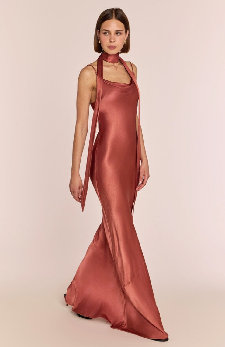 Woman wearing a rust-colored satin halter neck gown on a beige background