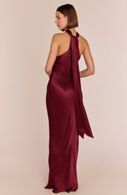 Burgundy halter neck gown on a model against a beige background