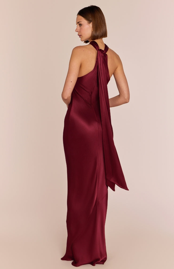 Burgundy halter neck gown on a model against a beige background