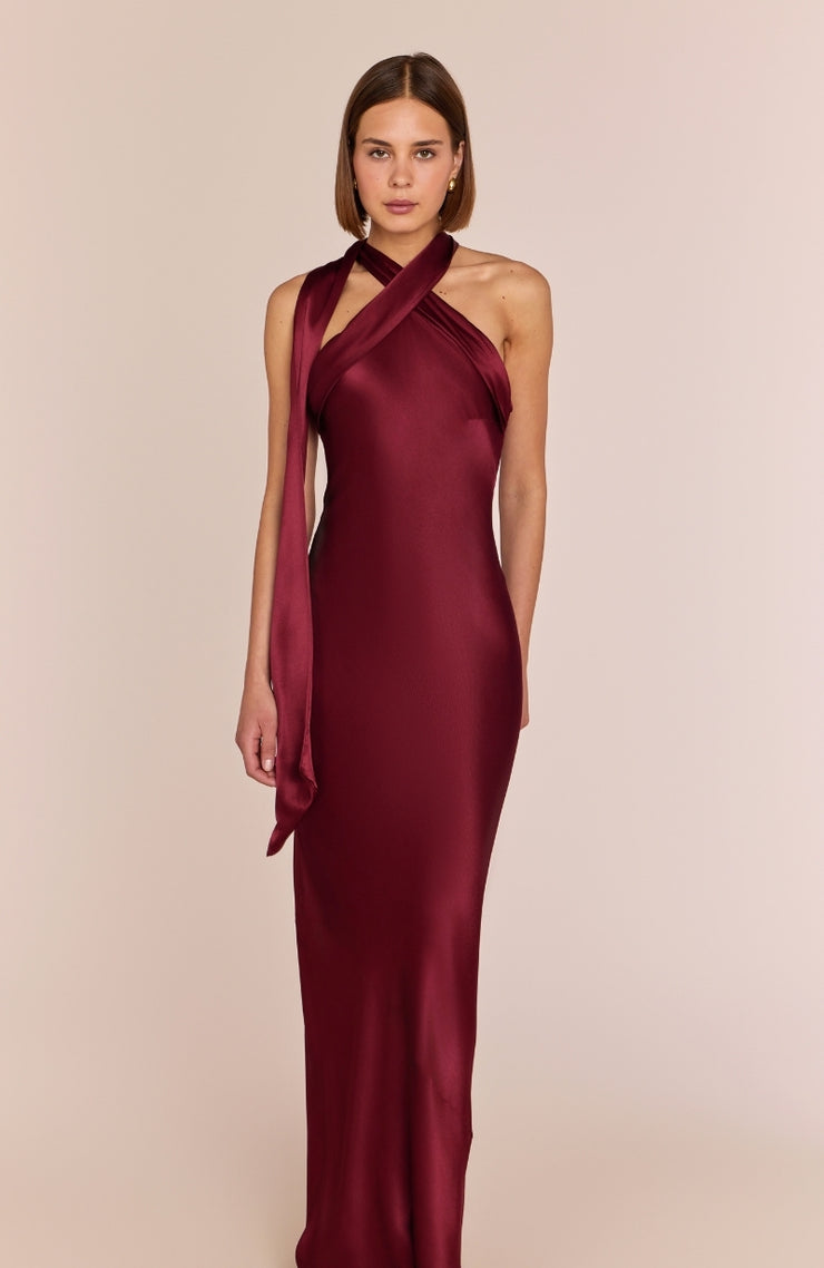 Burgundy satin halter neck gown on a model against a beige background