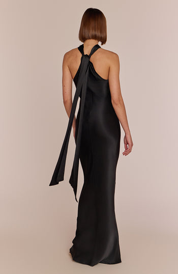 Woman wearing a black evening gown with a large bow detail on a beige background