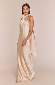 Woman wearing a long, flowing beige dress against a plain background