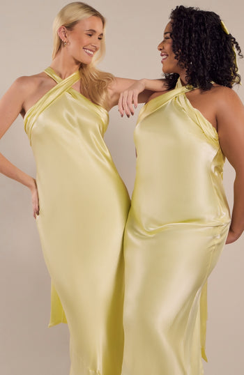 Two women wearing matching yellow satin dresses against a plain background