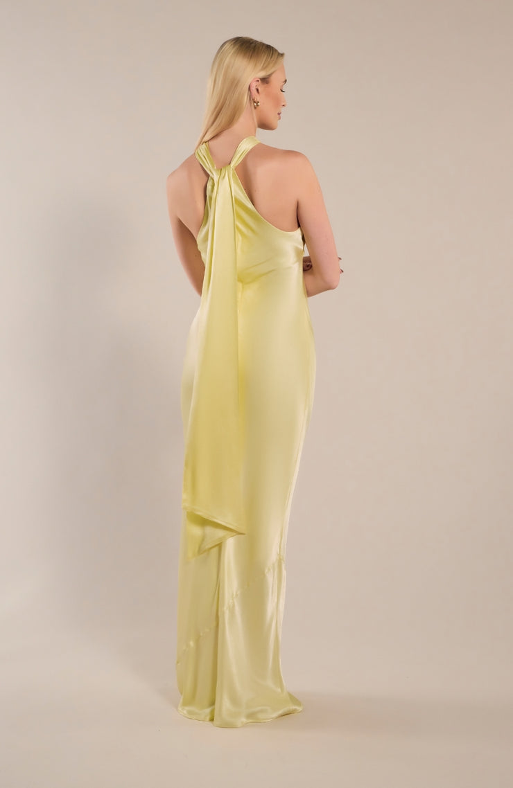 Woman wearing a light yellow halter neck dress against a plain background