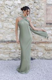 Woman in a green evening gown standing against a stone wall.