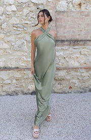 Woman in a green dress standing against a stone wall.