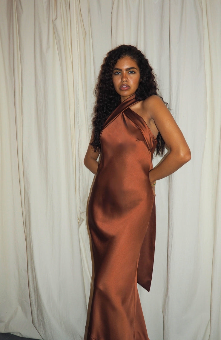 Woman wearing a brown satin dress against a white curtain background